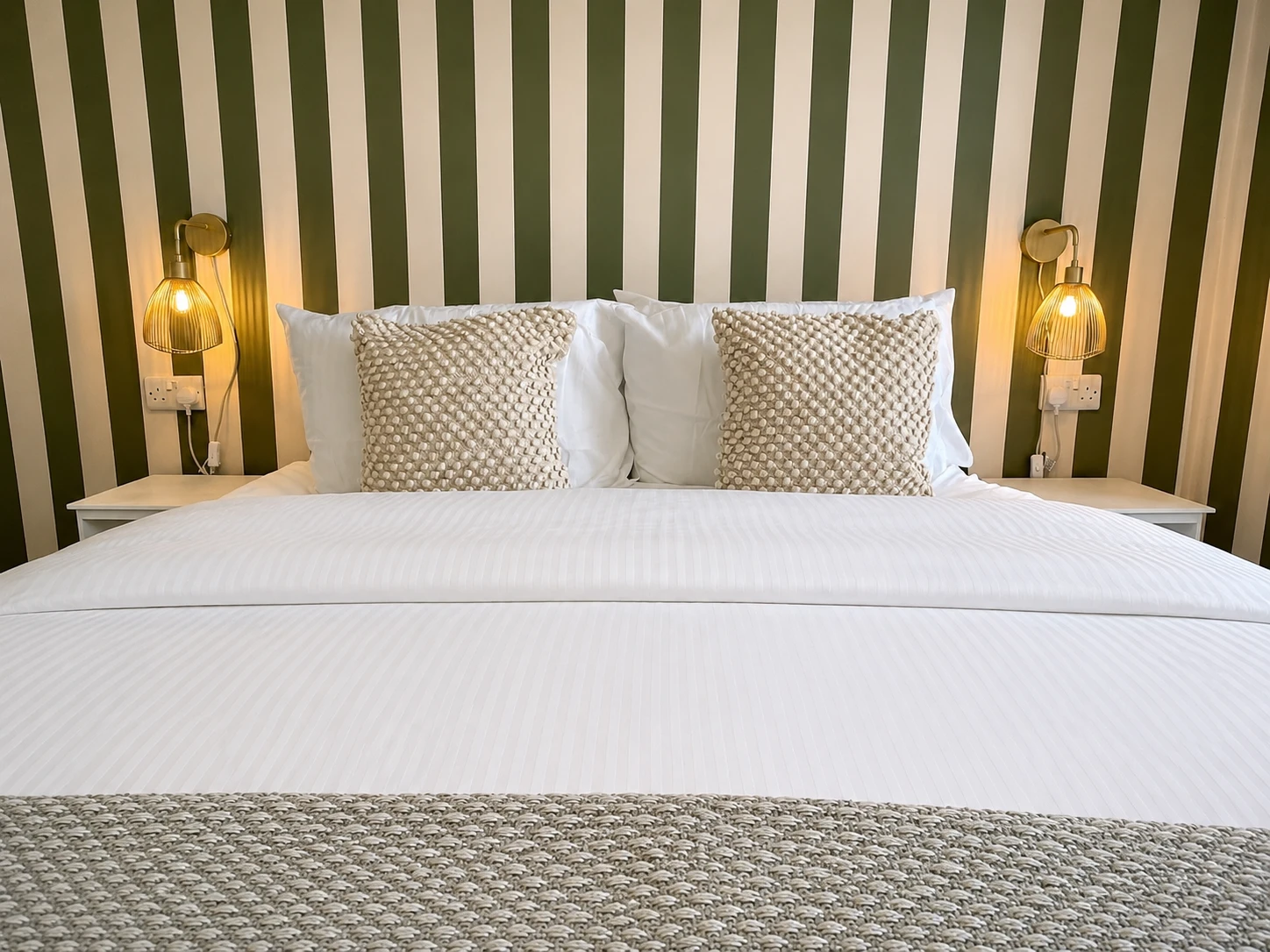 A bedroom with green striped wallpaper and brass wall lights, designed by Nomi Atelier